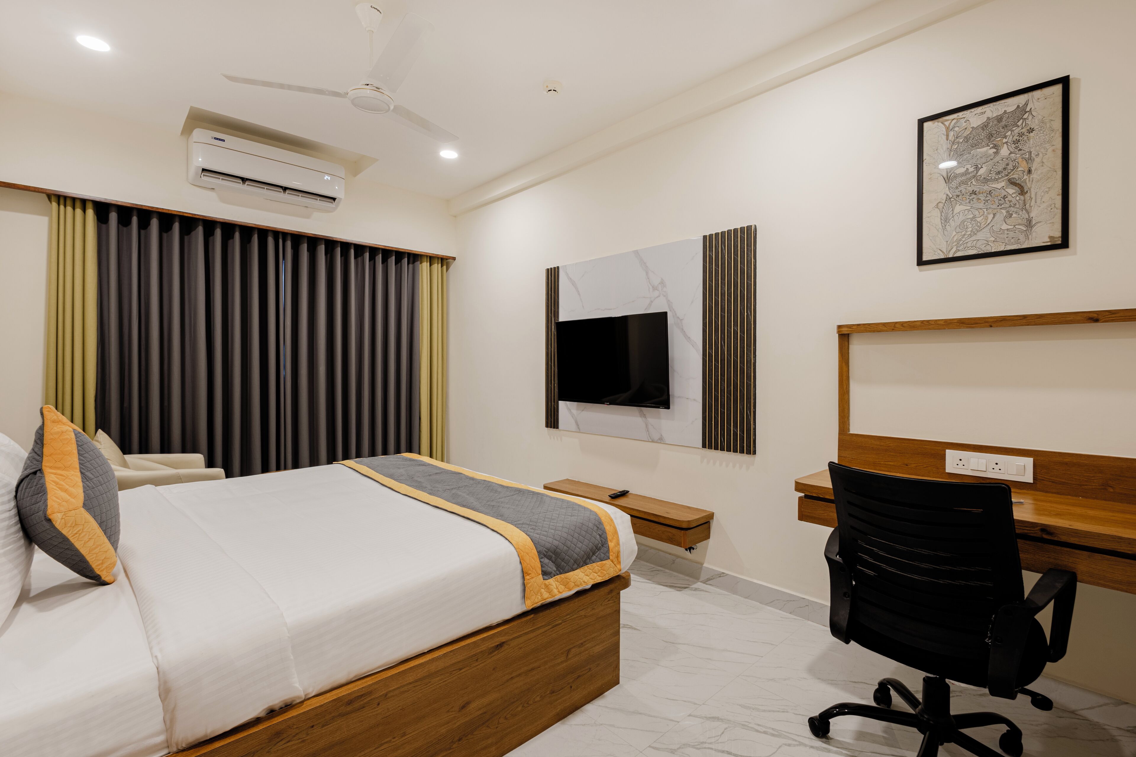 A hotel room with a bed, a desk, a chair, an air conditioner, a TV, and a ceiling fan.