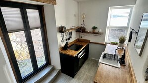 Eine kleine Küche mit einem schwarzen Herd, einer Holz Arbeitsplatte und einem Fenster mit Jalousien.
