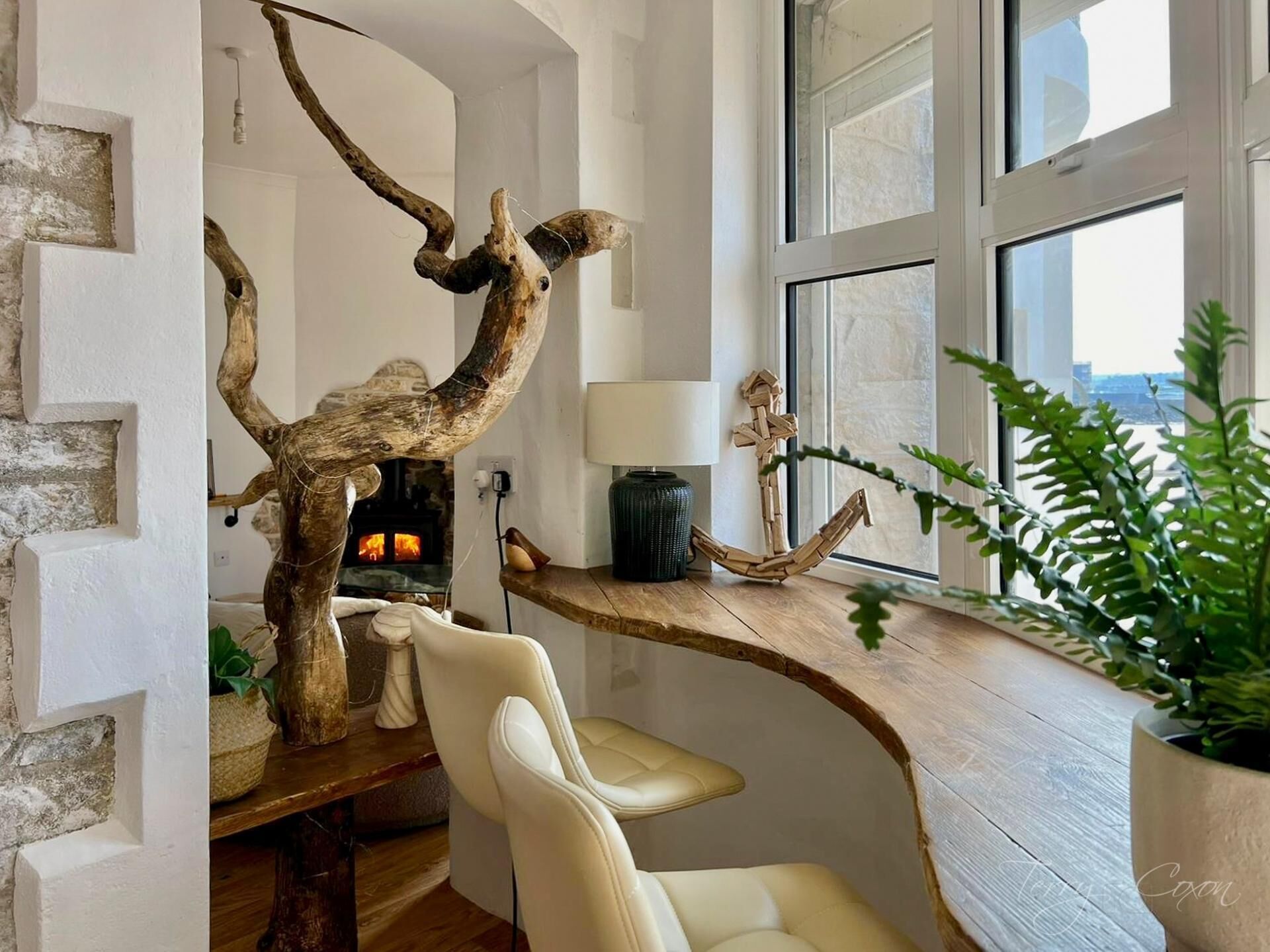 Ein modernes Interieur mit Kamin, einer Holzskulptur, einem Sessel und einem großen Fenster.