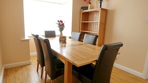 A dining area with a wooden table and chairs, a bookshelf, and a clock on the wall.