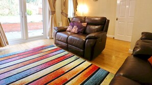 A living room with a leather sofa, a colorful striped rug, and a sliding glass door leading to an outdoor area.