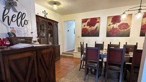 Un comedor con una barra de madera, un letrero que dice 'hello' y otro que dice 'welcome'. Hay cuadros de flores rojas en la pared y un suelo de baldosas.