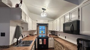 Una cocina con armarios blancos, estufa negra, microondas y encimera de piedra.