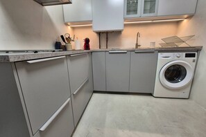 Eine moderne Küche mit grauen Schränken, einer integrierten Waschmaschine und einer Arbeitsplatte mit verschiedenen Küchenutensilien.