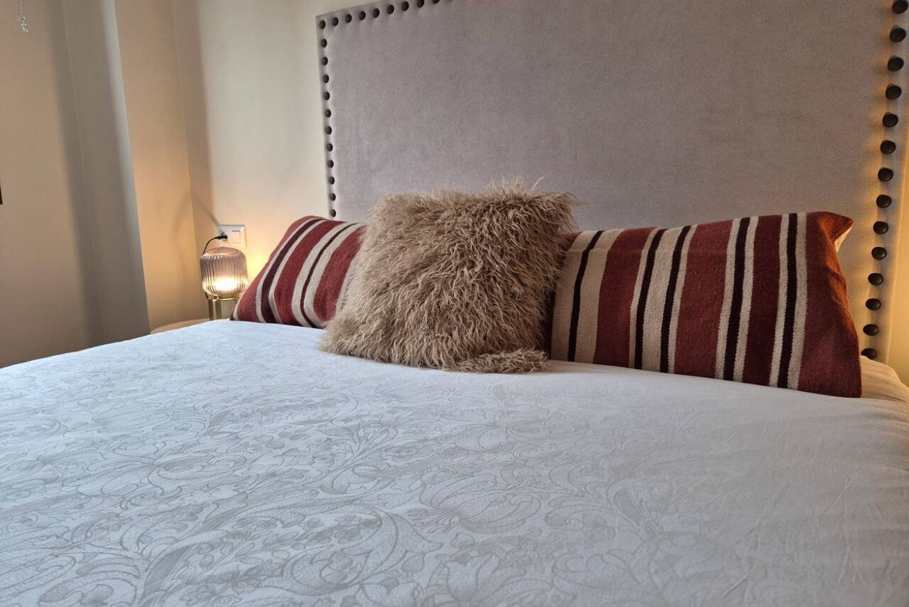 Una cama con cabecera capitonada, almohadas a rayas y una colcha estampada.