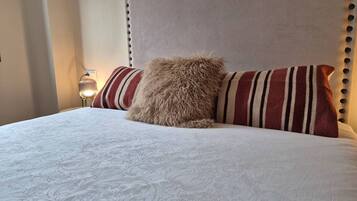 Una cama con cabecera capitonada, almohadas a rayas y una colcha estampada.