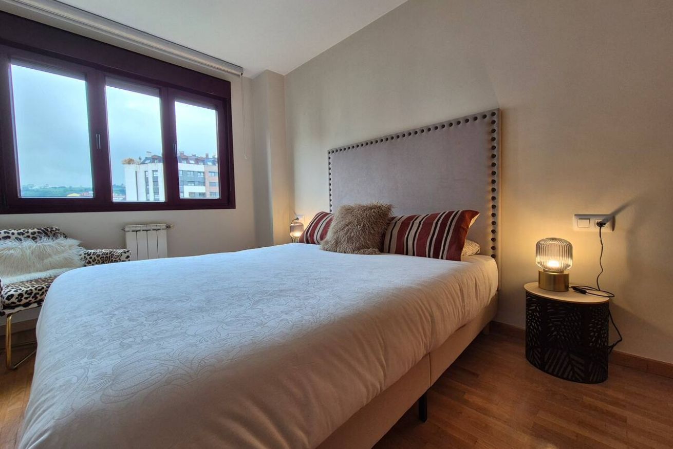 A bedroom with a large bed, a window with a view, a bedside table with a lamp, and a radiator.