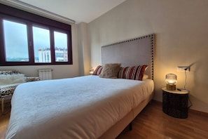 Un dormitorio con una cama grande, una ventana con vistas, una mesita de noche con lámpara y un radiador.