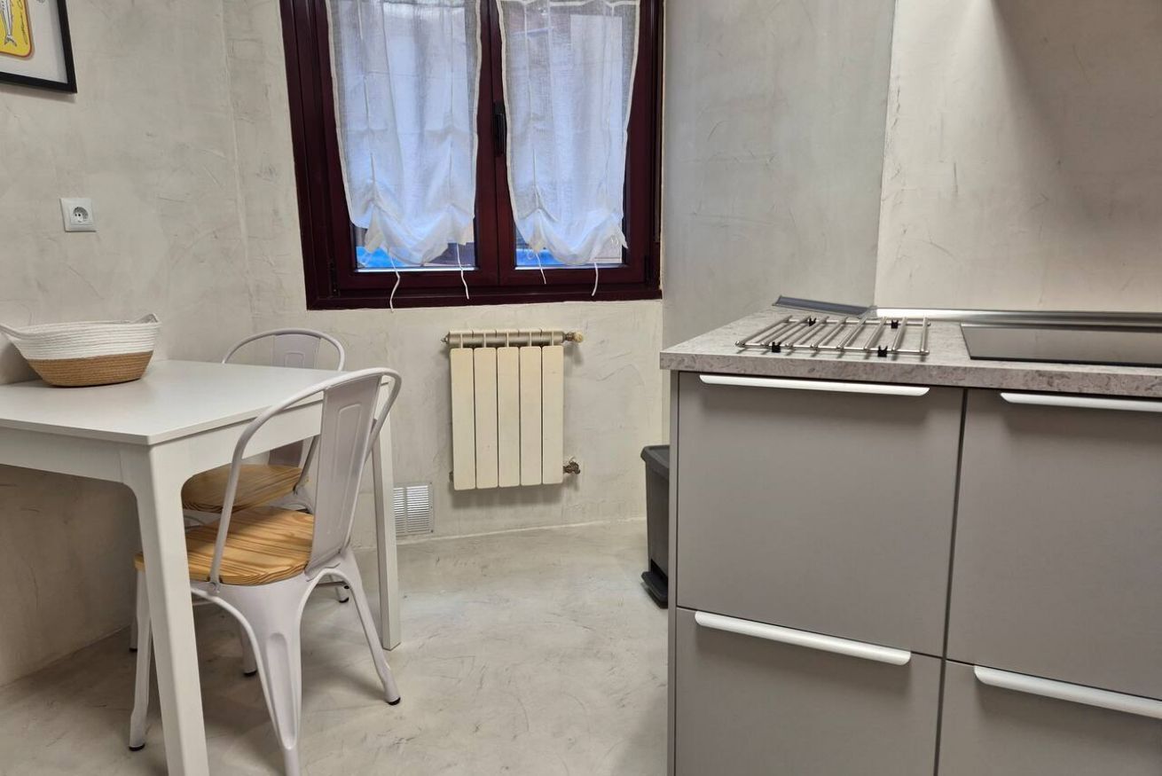 Una cocina con una mesa blanca, una silla, un radiador y una ventana con cortinas.