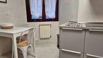 Una cocina con una mesa blanca, una silla, un radiador y una ventana con cortinas.