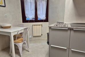 Una cocina con una mesa blanca, una silla, un radiador y una ventana con cortinas.