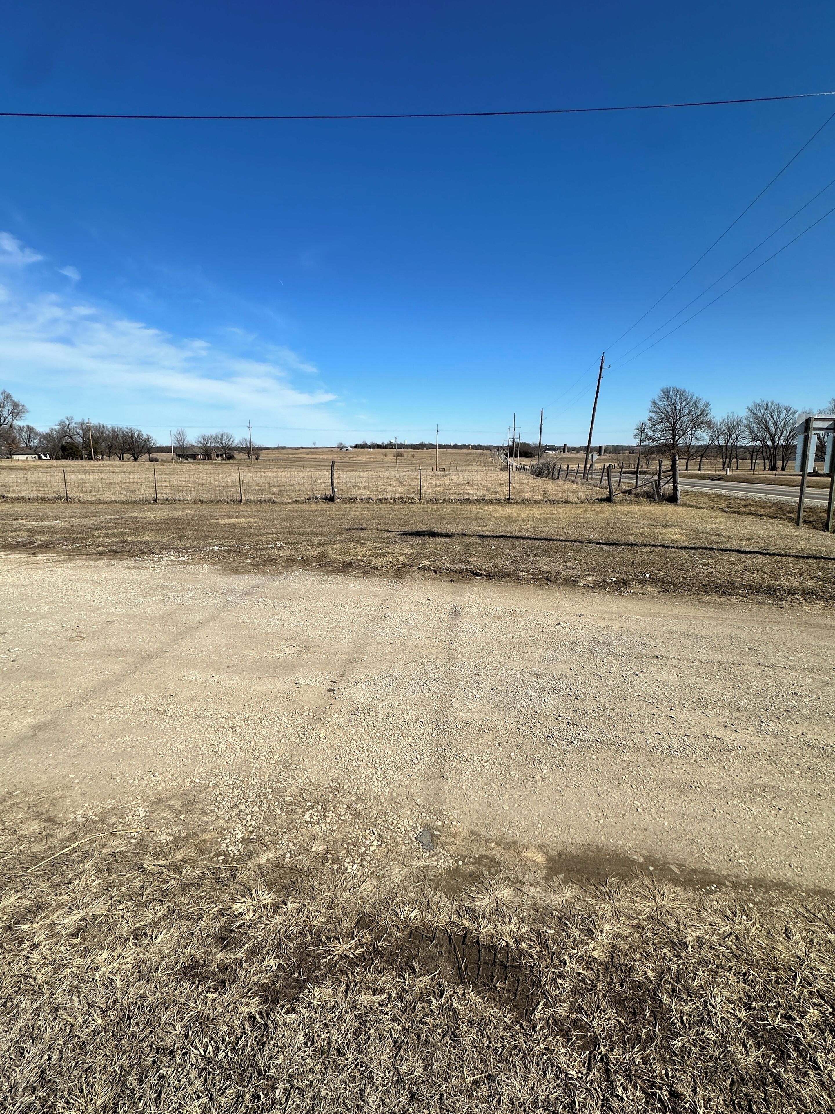 A vast, open field with a dirt road leading towards a small building.