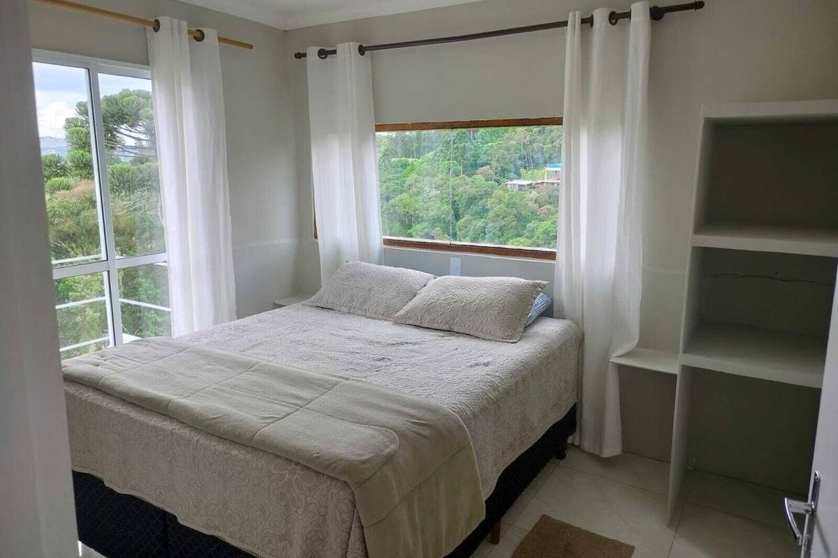 Une chambre à coucher avec un lit, une fenêtre avec des rideaux et une vue sur la verdure.