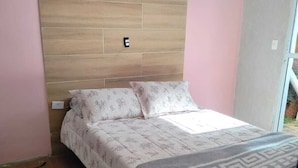 Une chambre avec une tête de lit en bois, un lit recouvert d’une literie à motifs floraux, un plaid à motifs et un petit tapis.