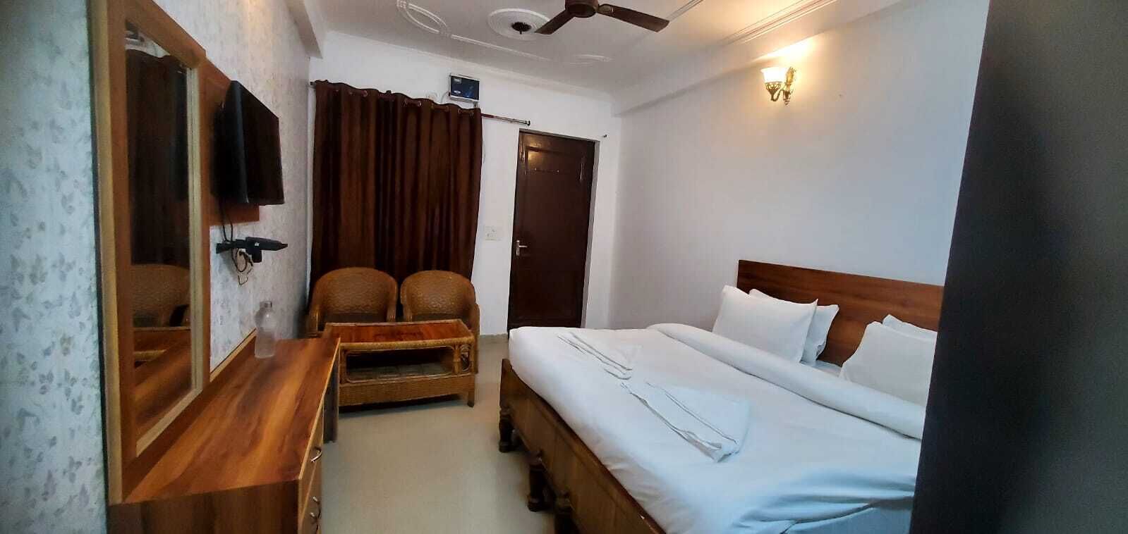 Ein Hotelzimmer mit einem Bett, einem Nachttisch aus Holz, einem Sessel, einem kleinen Tisch, einem Deckenventilator und einem an der Wand befestigten Fernseher.