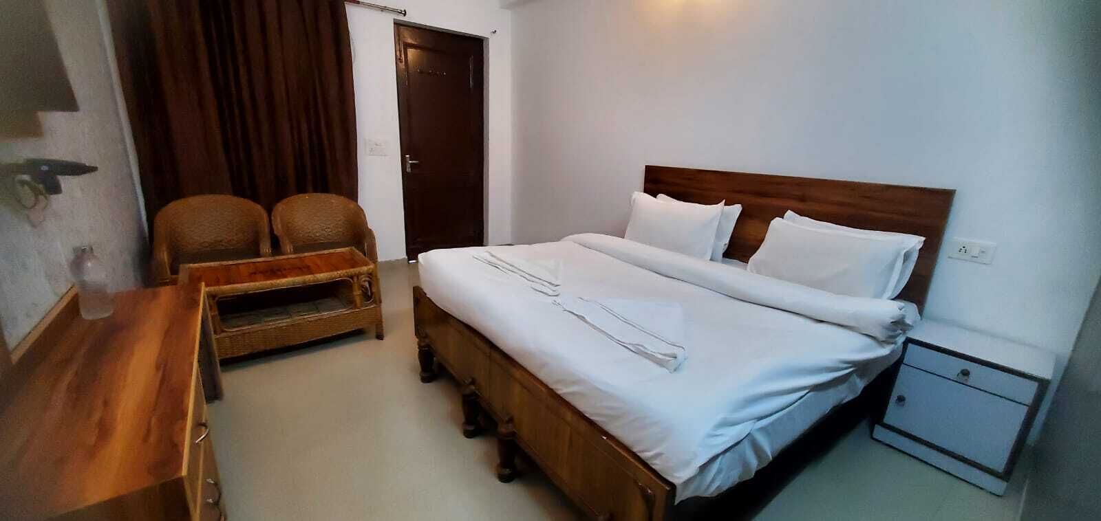 A hotel room with a wooden bed, white linens, a small wooden nightstand, a chair, and a door.
