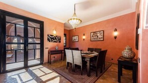 A dining area with a table set for four, a patterned rug, and wall-mounted lights. - Residence Dar Lamia Marrakech : 1 Bedroom Villa  (Dar Caïd Layadi)