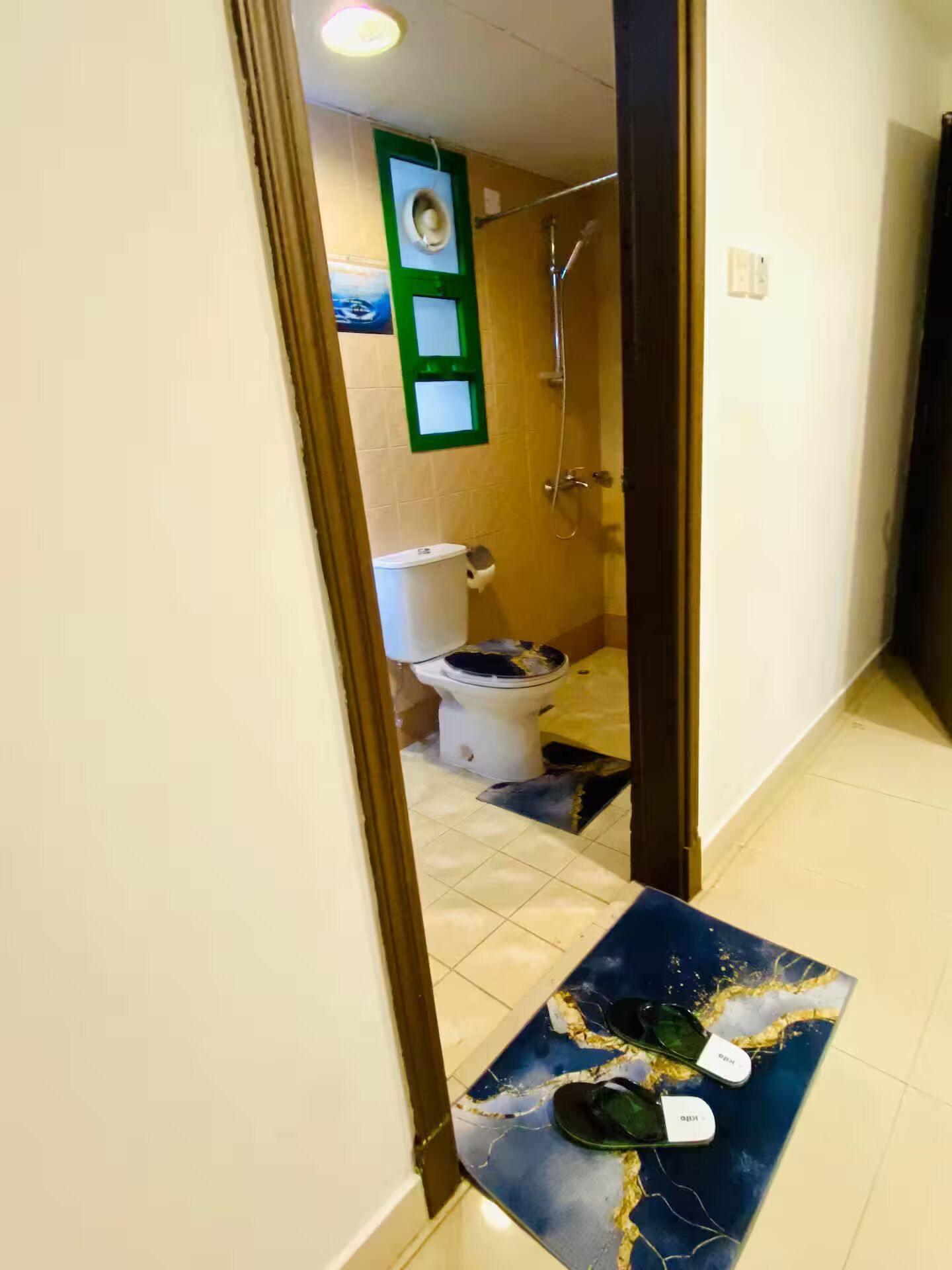 Un pasillo estrecho que conduce a un baño con inodoro, ducha y una pequeña mesa con gafas de sol y un sombrero.