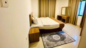 A modern hotel room with a neatly made bed, a wooden nightstand, a mirror, and a patterned rug. - Rest-Inn Two Bedrooms Apartment (Muscat)