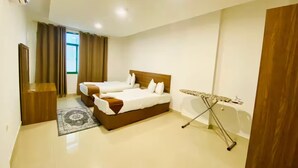 A hotel room with two beds, a small table, an ironing board, and a window with curtains. - Rest-Inn Two Bedrooms Apartment (Muscat)