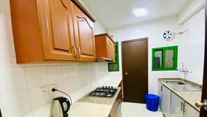 A compact kitchen with wooden cabinets, a gas stove, a kettle, and a sink. - Rest-Inn Two Bedrooms Apartment (Muscat)