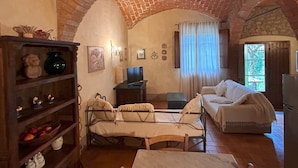 A rustic room with a brick ceiling, a bed, a sofa, a television, and a shelf with decorative items. - Appartamento Vele, Wifi, Near Perugia (Monteleone d'Orvieto)