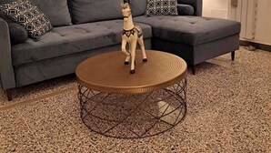 A living room with a grey sofa, patterned cushions, a world map on the wall, a small decorative horse statue, and a textured floor.