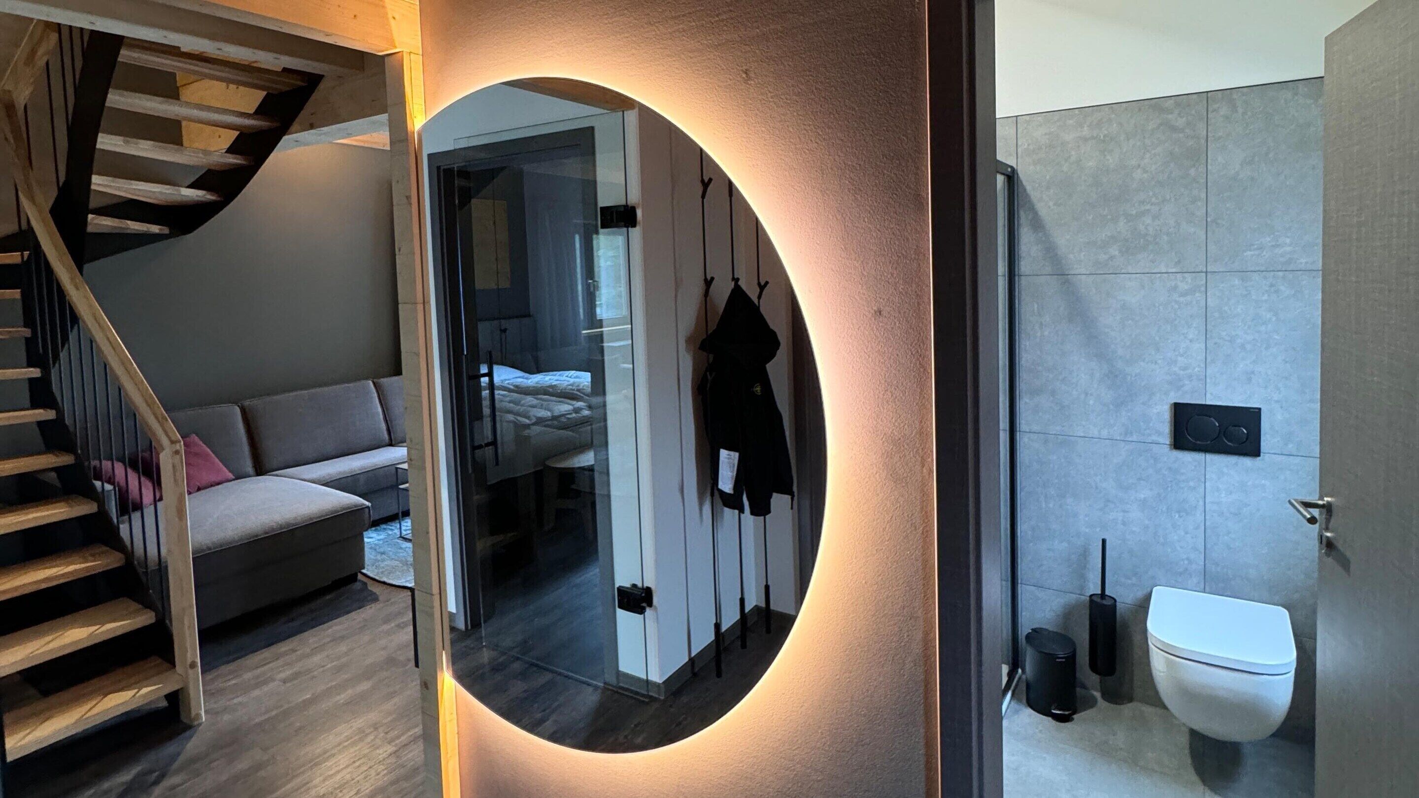 Une chambre moderne avec un escalier, un canapé, un lit et une salle de bain équipée de toilettes et d’une poubelle.
