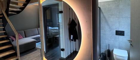 Une chambre moderne avec un escalier, un canapé, un lit et une salle de bain équipée de toilettes et d’une poubelle.
