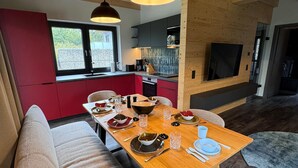 A modern kitchen with red cabinets, a dining area with a wooden table set for four, and a large TV mounted on a wooden wall. - Modernes Chalet in Hahnenklee (Goslar)