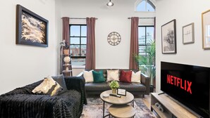 A modern living room with a sofa, coffee table, and a flat-screen TV displaying "NETFLIX". - The Hallmark 3BR Apt JQ Birmingham, Parking & WiFi (Birmingham)