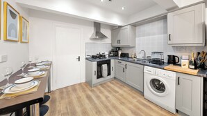 A modern kitchen with grey cabinets, a built-in oven, a washing machine, and a dining area with a table set for four. - The Hallmark 3BR Apt JQ Birmingham, Parking & WiFi (Birmingham)