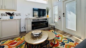 Une cuisine moderne dotée d’un téléviseur à écran plat, d’un coin repas agrémenté d’un tapis coloré et d’une grande fenêtre avec des stores.