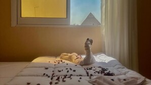 A bedroom with a bed, a window with a view of a pyramid, and a swan decoration on the bed. - kings pyramids view inn (Giza)