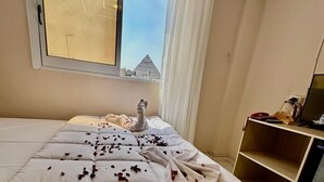 A hotel room with a large bed, a window with a view of a pyramid, and a desk with a computer and phone. - kings pyramids view inn (Giza)