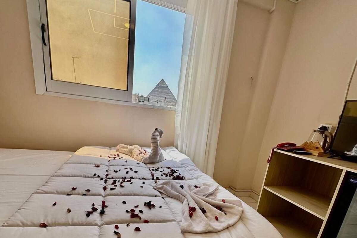A hotel room with a large bed, a window with a view of a pyramid, and a desk with a computer and phone.