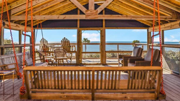 Une terrasse en bois avec une balançoire, des fauteuils en osier et une vue sur l’océan.