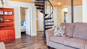 Un salon moderne avec un escalier en colimaçon, un plancher en bois, un canapé agrémenté de coussins à motifs et une étagère rouge.