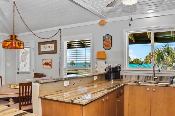 A kitchen with a marble countertop, wooden cabinets, a sink, and a window with a view of the ocean.