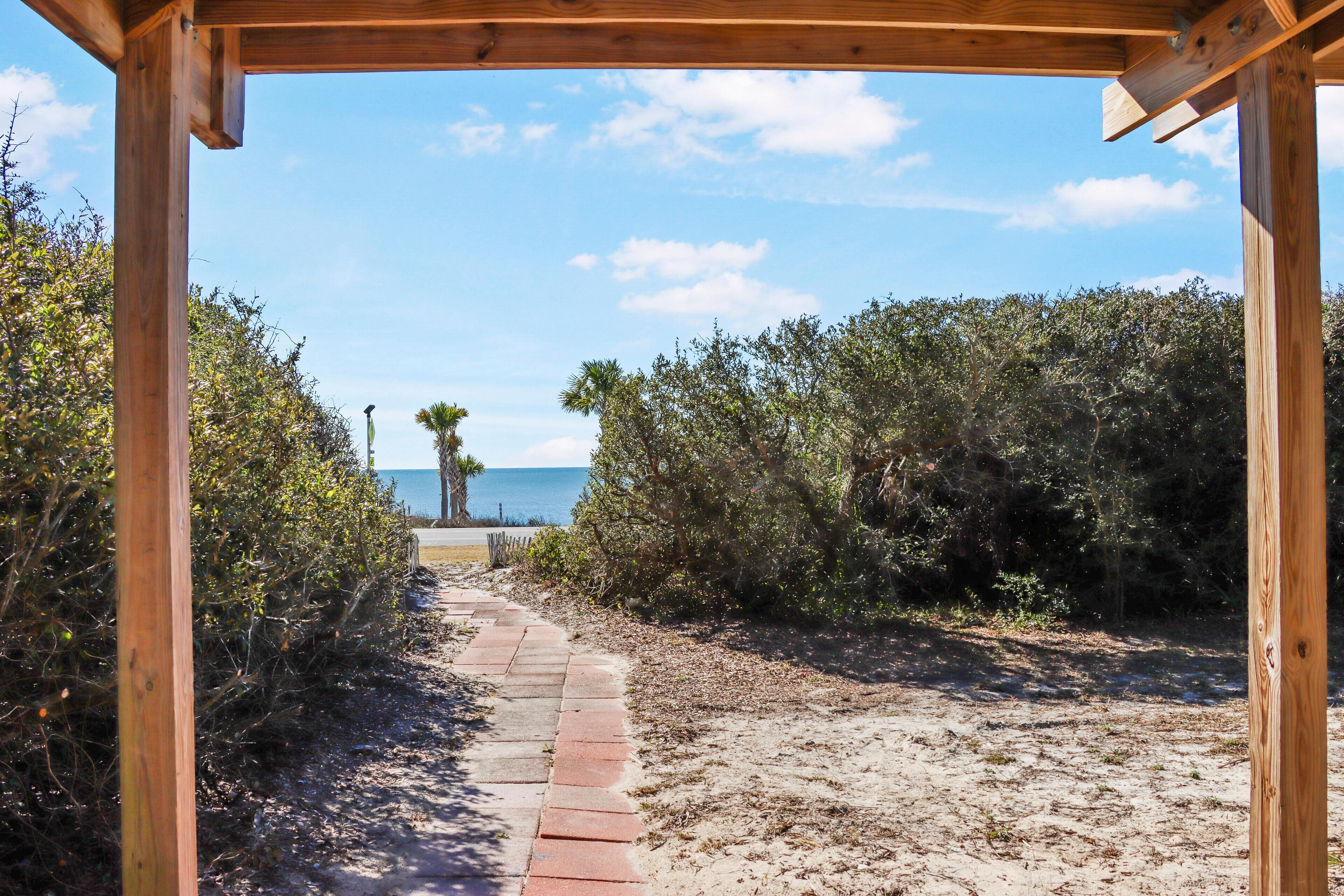 Una pérgola de madera con un camino que lleva a la playa.