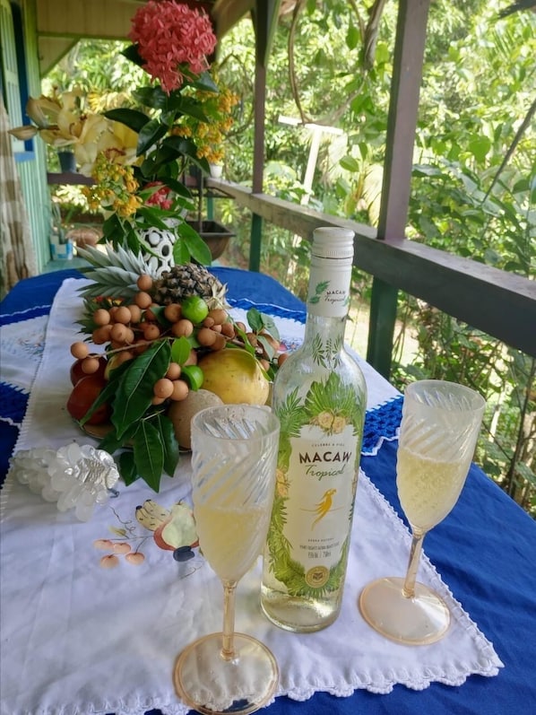 A table with a bottle of Macaw Tropical, two glasses of a light-colored beverage, and a variety of tropical fruits and flowers. - Mermaid Hotel Amazon  (Presidente Figueiredo)