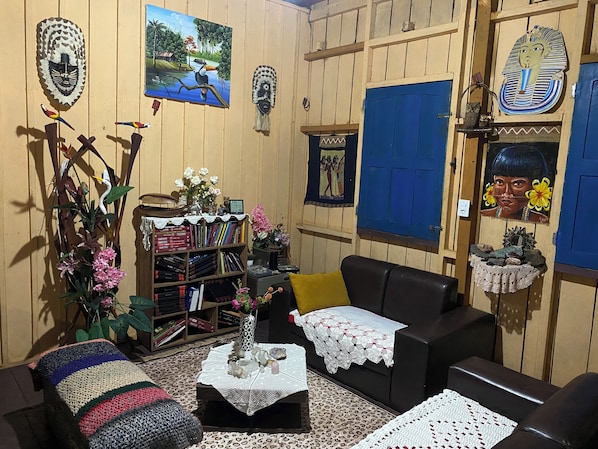 Una sala de estar acogedora con una estantería, un sofá, una mesa de centro con objetos decorativos y decoración de pared que incluye un cuadro y adornos con motivos egipcios.