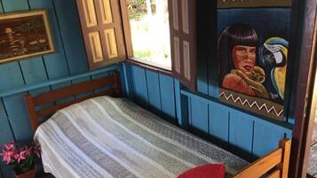 Una cama individual con una colcha a rayas, un almoháron rojo y una ventana con vistas a la vegetación.