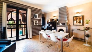 A modern dining area with a white table and chairs, a fireplace, and a view of an outdoor pool. - Residence Dar Lamia Marrakech : 2 Bedroom Villa with Private Pool (Dar Caïd Layadi)
