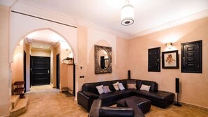 A spacious living area with a black sectional sofa, a large mirror, and a framed picture on the wall. - Residence Dar Lamia Marrakech : 2 Bedroom Villa with Private Pool (Dar Caïd Layadi)