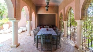 A covered patio area with a table and chairs, surrounded by arches and columns, and a hanging lantern above. - Residence Dar Lamia Marrakech : 2 Bedroom Villa with Private Pool (Dar Caïd Layadi)