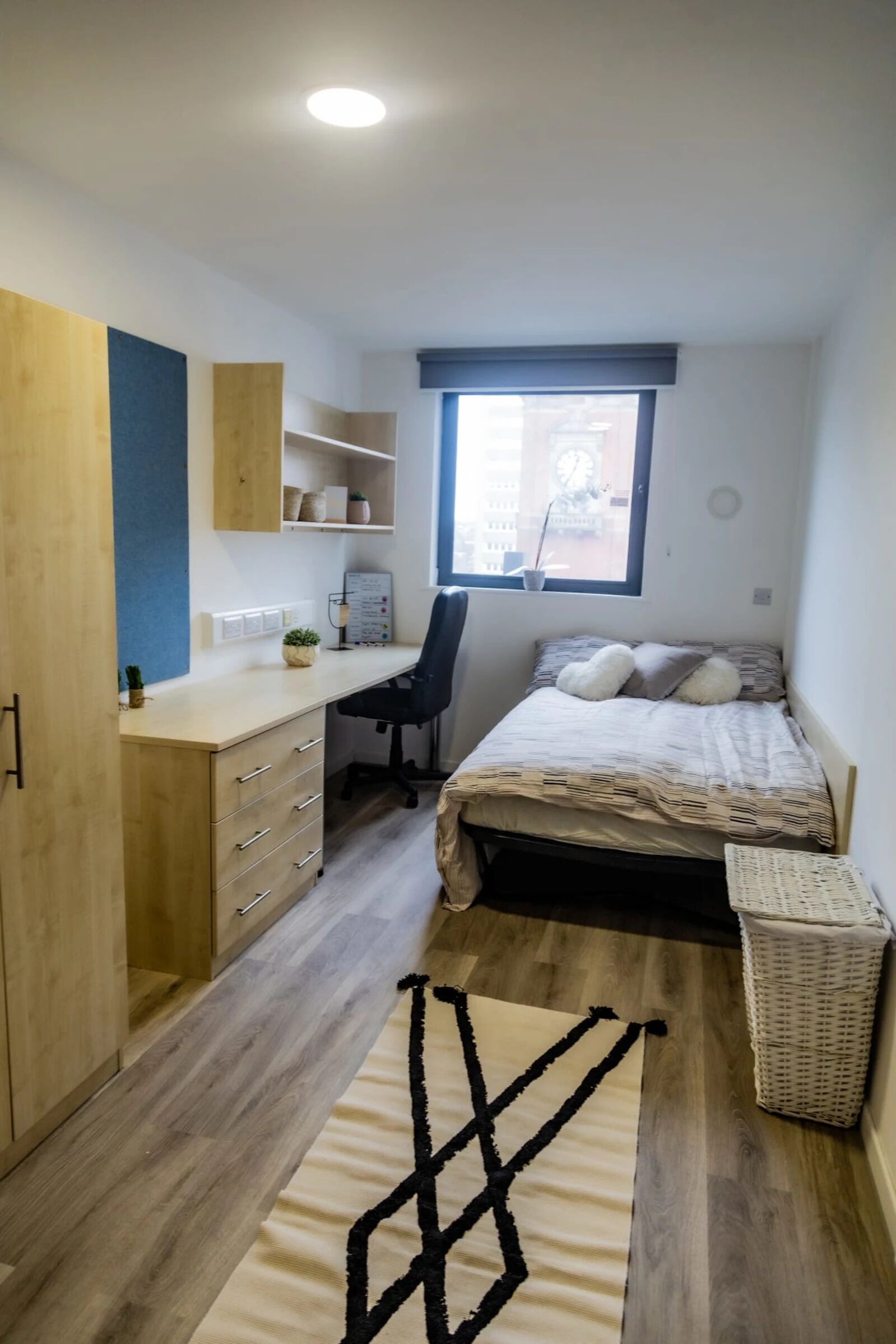 A compact bedroom with a bed, desk, chair, and a small window.