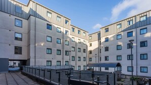 Ein modernes Mehrfamilienhaus mit mehreren Stockwerken, großen Fenstern und einer überdachten Außenbereich mit Tischen und Bänken.