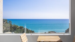 Un balcón con mesa y sillas de madera, con vista al mar y un cielo despejado.