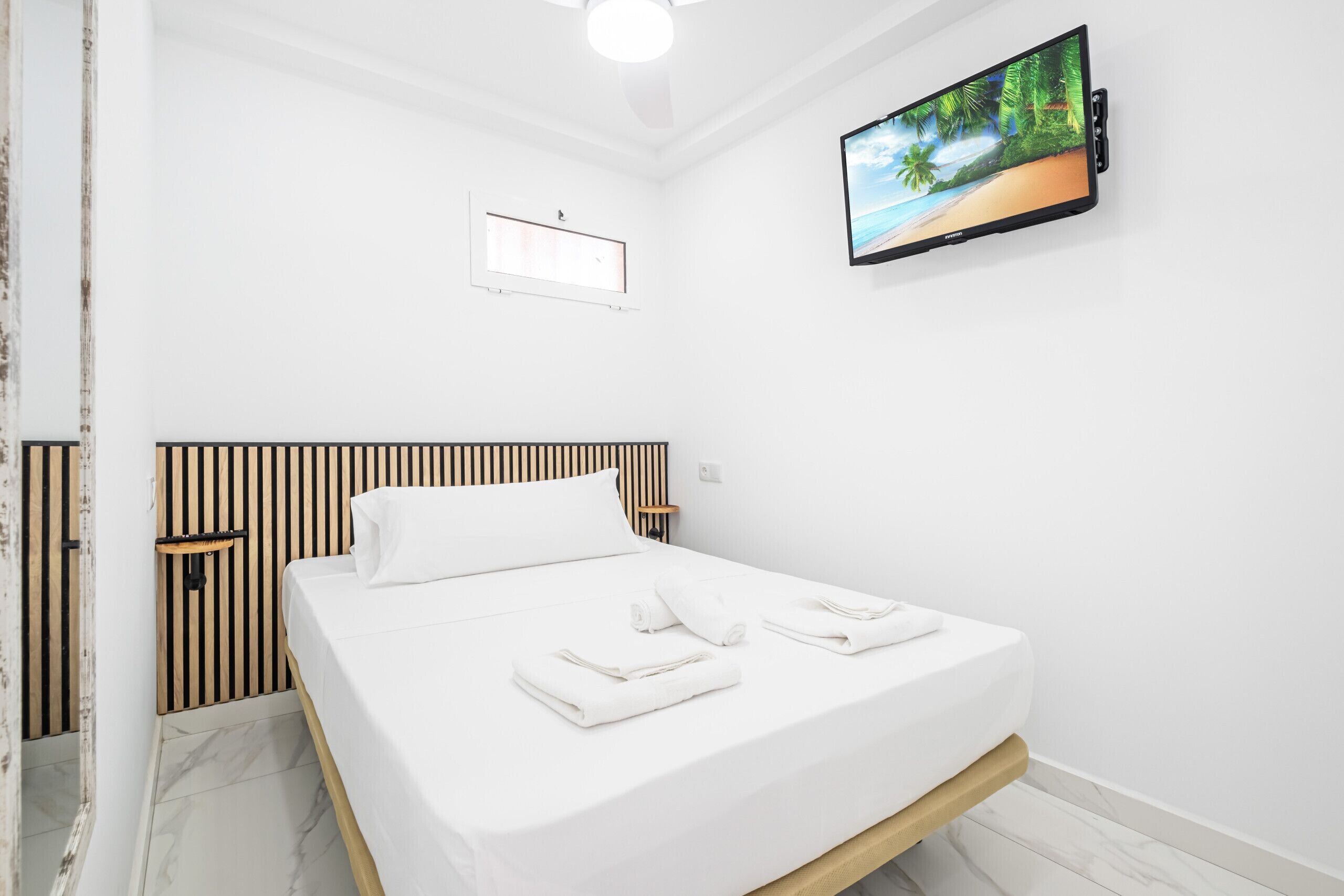 Una habitación de hotel con una cama, un televisor instalado en la pared y una ventana con persianas.